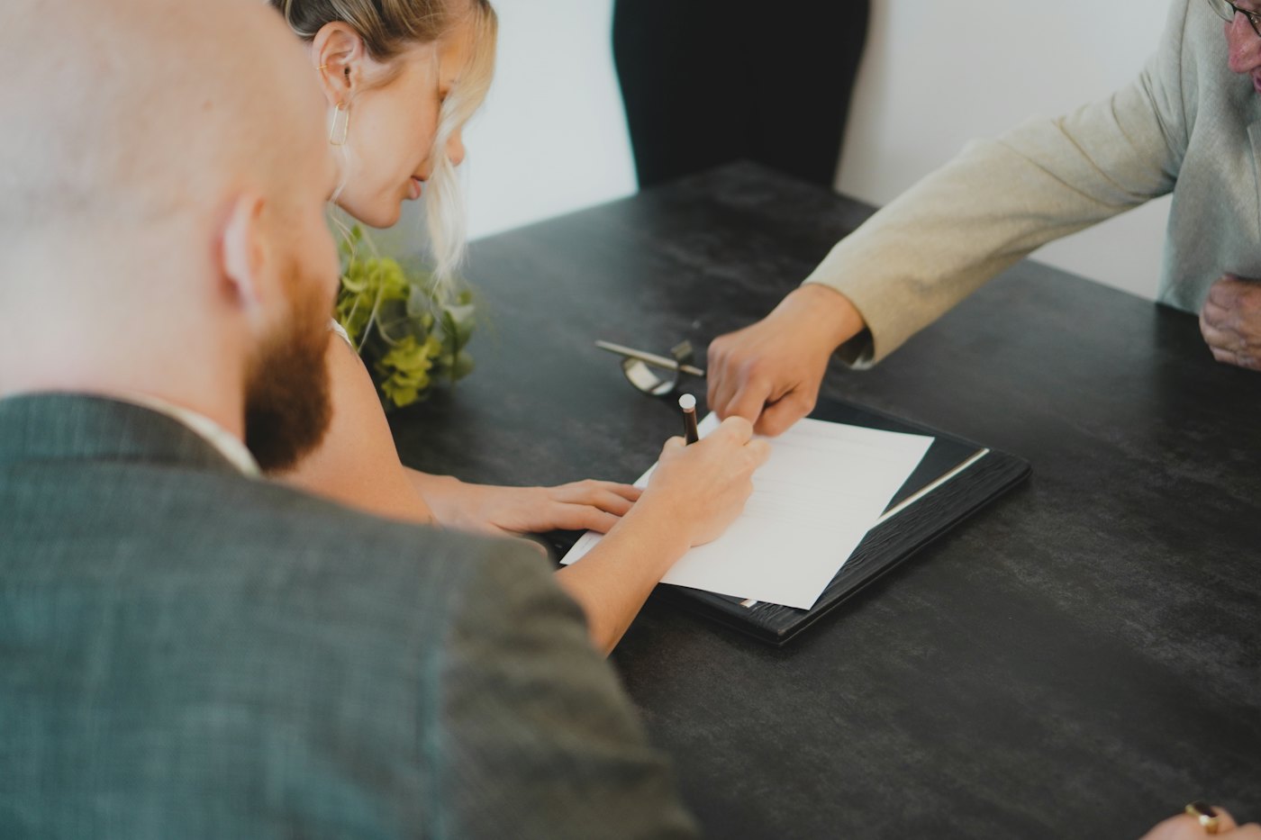 Two people at a desk, one signing a document